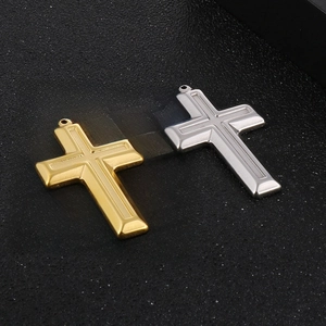Polished gold and silver stainless steel cross pendants on a textured black surface