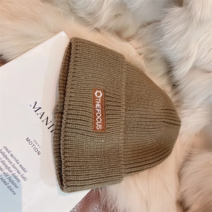 Detail of a dark khaki knitted beanie with focus patch on soft faux fur background