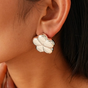 Macro shot of polished silver flower earrings with five petals on a model's ear