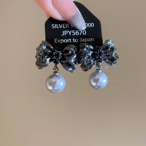 Gros plan de boucles d'oreilles nœud en métal noir avec cristaux noirs et pendentif perle