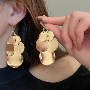 Detail of gold layered leaf sequins dangle earrings worn by a model on blurred background