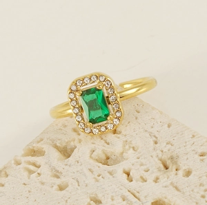Macro shot of gold square emerald green zircon ring on a beige stone pedestal