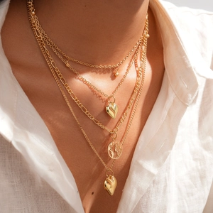 Detail of layered gold necklaces with heart and embossed world map pendants on a model