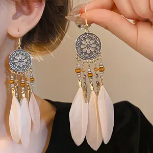 Dettaglio di orecchini boho con nappe, piume dorate e perline di legno colorate