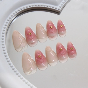 Pink gradient almond press-on nails with 3D embossed flowers and gold beads on a mirror tray