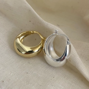 Thick oval hoop earrings in gold and silver finish on soft textured beige fabric