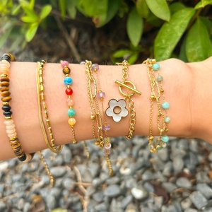 Layered gold chain bracelets with natural stones and white shell flower charm on wrist