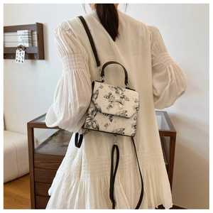 Rear view of model wearing white butterfly print backpack with silver bow buckle