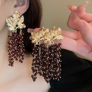 Detailed close-up of long tassel earrings with golden leaf and dark red grape beads
