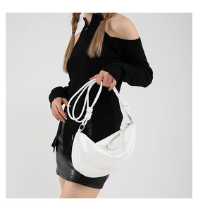 Detail of white patent leather crescent bag with unique twisted knot shoulder strap design