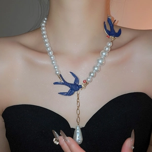 Close-up of pearl necklace with blue bird charm and drop pendant on a model