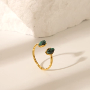 Dettaglio di un anello dorato aperto con due pietre naturali verdi a goccia su roccia bianca