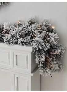 Detail of flocked Christmas garland with pine cones, red berries and warm LED lights