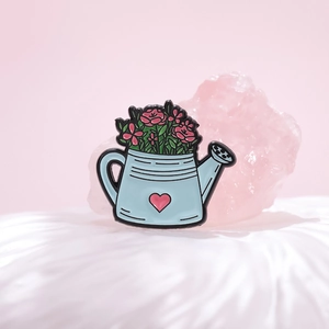 Broche en émail arrosoir bleu avec fleurs roses sur un fond dégradé rose doux