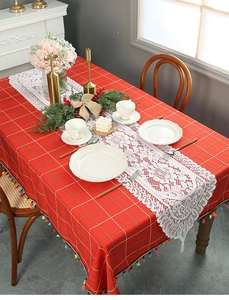 Detail of red checkered tablecloth with colorful tassels and white lace table runner