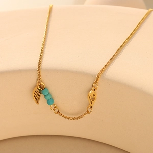 Gold wing turquoise anklet on a ceramic beige background with soft natural lighting