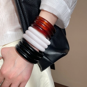 Close-up of triple-layered geometric resin bangles in amber brown, white, and black