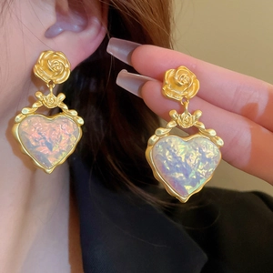 Détail de boucles d'oreilles fleur en métal doré avec pendentif cœur en résine nacrée