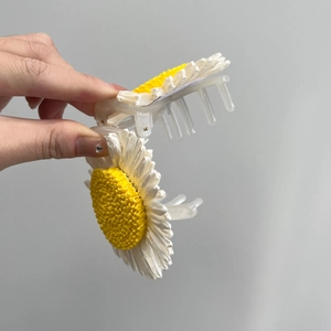 Detailed close-up of large white and yellow daisy hair claw clip with woven texture