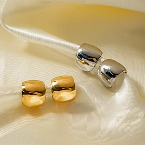 Close-up of polished gold and silver square hoop earrings on elegant beige silk