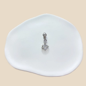 Close-up of a silver heart-shaped planetary navel ring with zircon on a ceramic dish