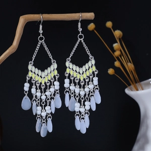 Dettaglio macro di orecchini boho argentati con perline gialle e bianche su legno
