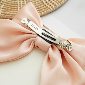 Detailed view of handmade pink satin bow hair clip with metal spring clasp on straw hat