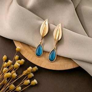Detail of golden leaf earrings with dark blue teardrop pendants on a wooden stand