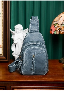 Close-up of gray-blue washed PU leather sling bag with multi-zipper pockets and texture