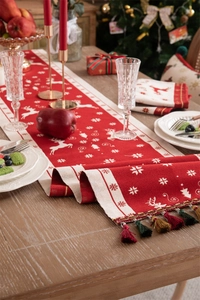 Detail of red Christmas table runner with white reindeer motifs and tassel trim