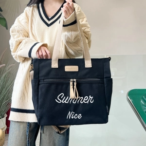 Detail of black canvas tote bag showing Summer Nice embroidery and leather logo tag