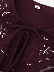Detail of burgundy ribbed knit shirt featuring intricate floral embroidery and white beadwork