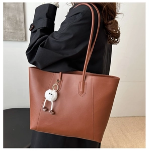 Detail view of brown faux leather tote bag with a white plush monster charm accessory