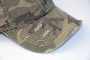 Detail of distressed camouflage baseball cap featuring worn edges and reinforced stitching