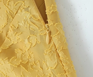 Makrodetail eines gelben Fishtail-Kleides mit Jacquard-Struktur und verdecktem Reißverschluss
