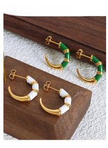 Detail showing white and green enamel C-shaped bamboo hoop earrings on dark wood