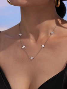 Close-up of a silver clover flower necklace with star charms on model neck