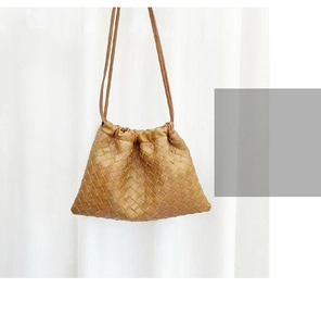 Detail of a brown woven leather drawstring bucket bag hanging by a window with natural light