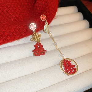 Macro shot of asymmetric gold earrings with red enamel wedding symbols and tiny pearls