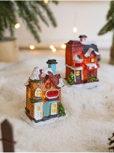 Close-up of LED glowing miniature resin Christmas houses on snow with warm lights