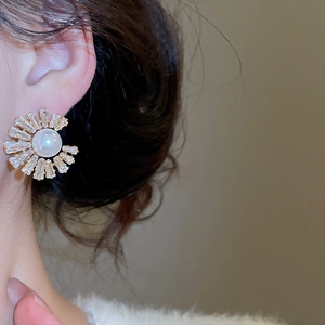 Detail view of sunflower pearl stud earring with zircon accents on female ear