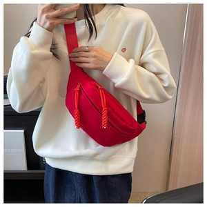 Detail of red canvas chest bag featuring dual zippers with woven rope pullers and wide strap