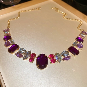Close-up of golden necklace with large purple and pink crystals on textured tray