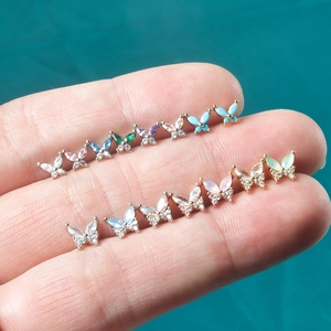 Miniature butterfly zircon stud earrings in various colors held in hand against green back
