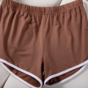 Detailed flat lay of brown yoga shorts featuring elastic high waist and white piping
