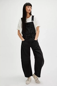 Detail of black denim overalls with adjustable metal buckles and chest pocket on a model
