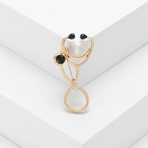 Gold stethoscope brooch with black gemstones on a minimalist white background