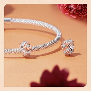 Close-up of a silver woven bracelet featuring rose gold flower charms with inlaid crystals
