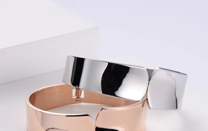 Detail of mirror-polished wide open bangles in silver and rose gold on a minimalist stand