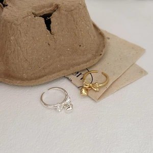 S925 sterling silver open ring with gold bow and heart charm on minimalist surface